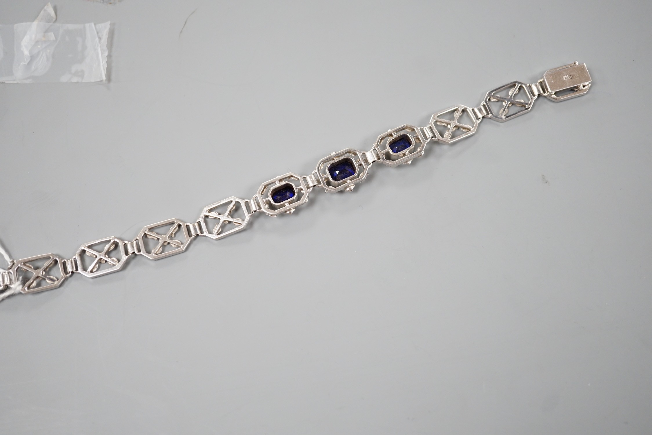 A modern 9ct white metal and three stone emerald cut synthetic sapphire set pierced link bracelet, approx. 18cm, gross weight 16.7 grams.